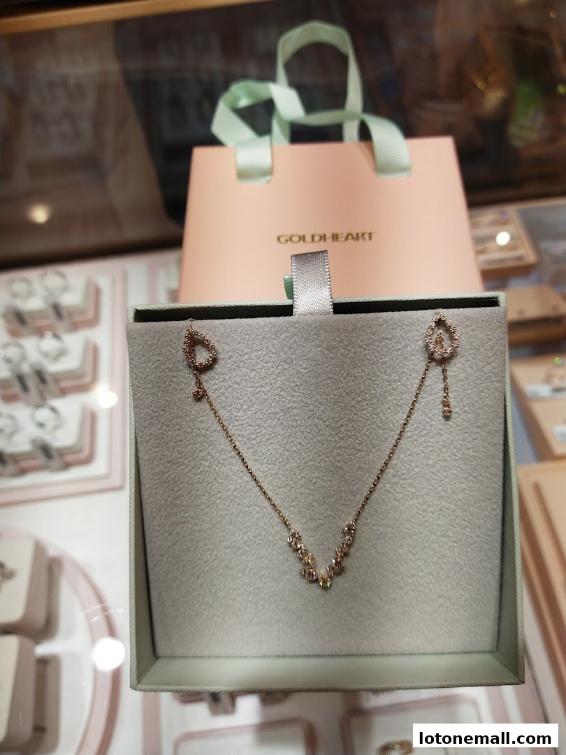 A delicate gold necklace with diamond accents displayed in a jewelry box with a Goldheart shopping bag.