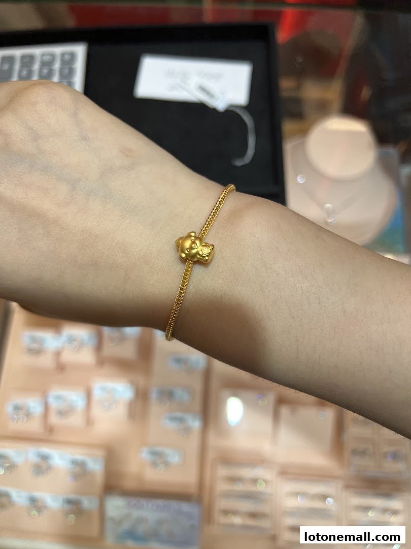A person's arm wearing a delicate gold bracelet with a cute teddy bear charm.