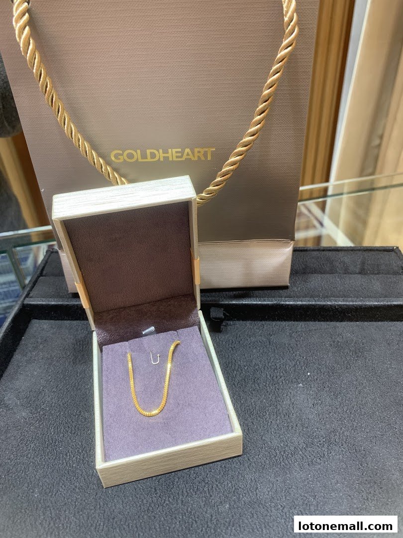 A gold chain necklace displayed in an open jewelry box with a Goldheart shopping bag in the background.