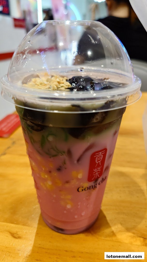 A close-up of a layered bubble tea drink with various toppings in a clear plastic cup.