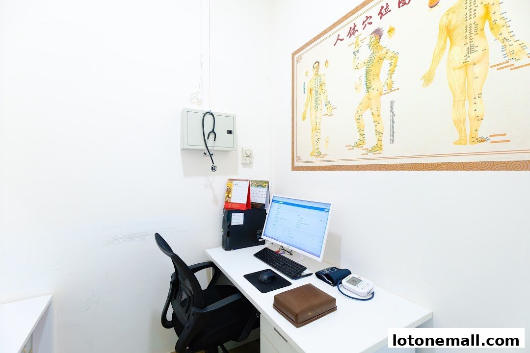 A desk with a computer, stethoscope, and acupuncture chart in a clinic.