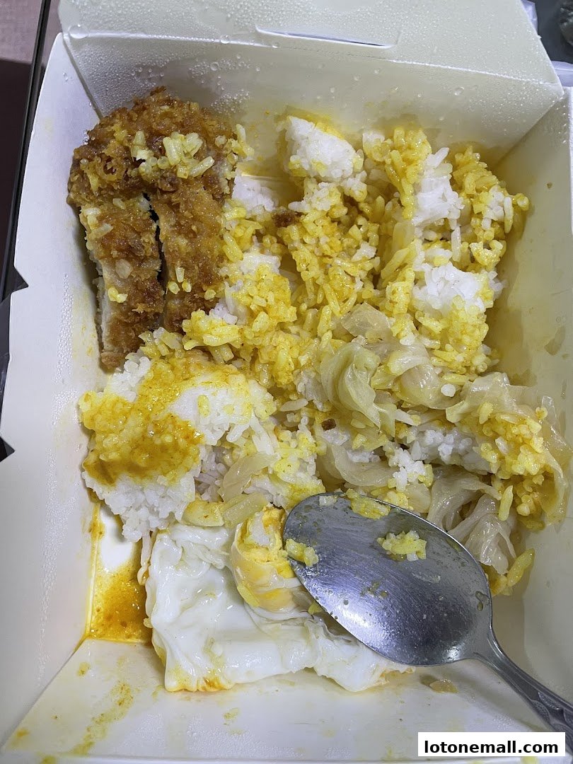 A takeout box filled with Hainanese curry rice, fried chicken, and a fried egg.