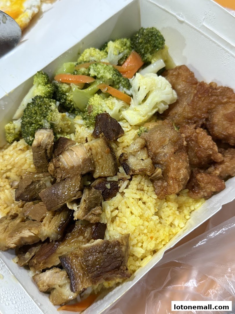 A takeaway box filled with Hainanese curry rice, braised pork, fried chicken, and mixed vegetables.
