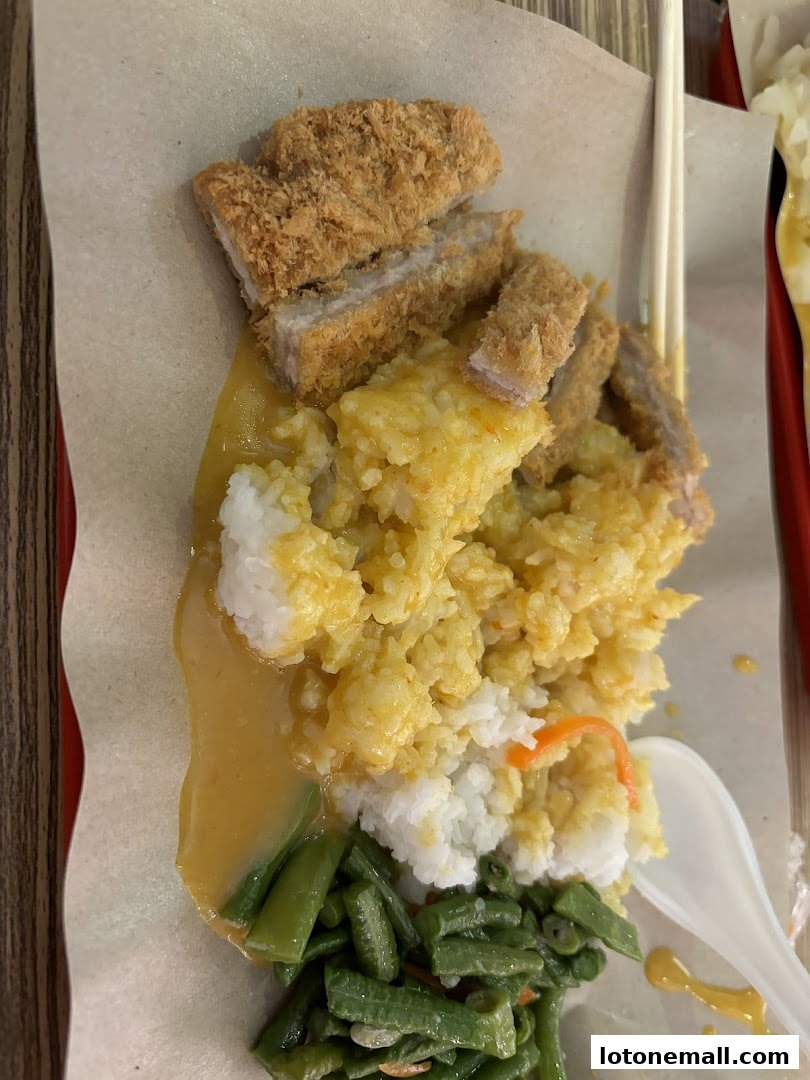 A plate of Hainanese curry rice with crispy fried pork, rice, green beans, and curry sauce.