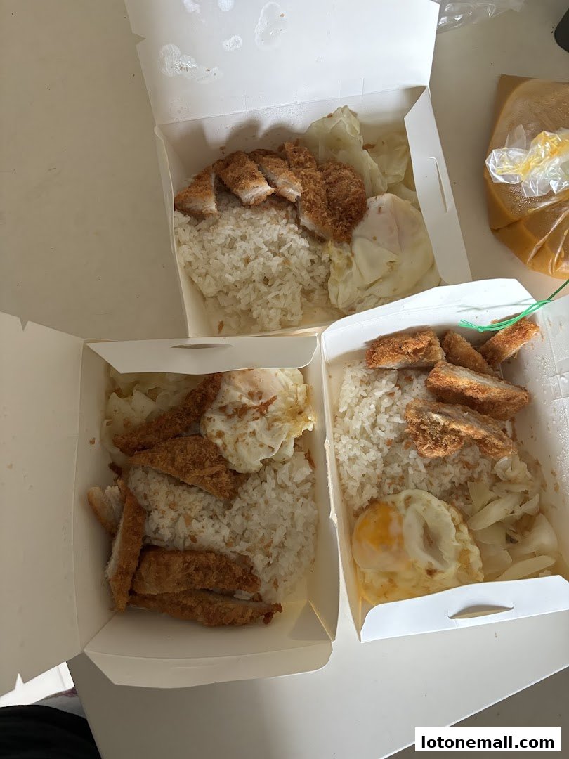Three takeaway boxes filled with Hainanese curry rice, fried chicken, and fried eggs.