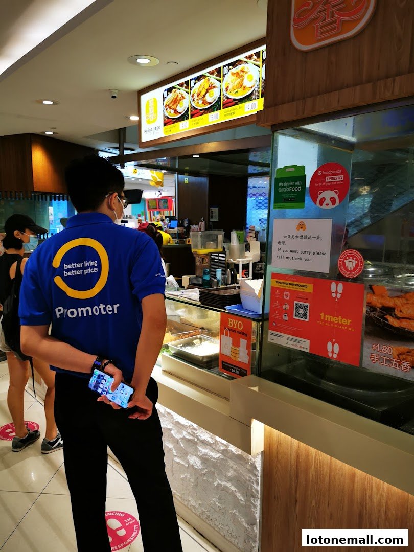 A person in a blue shirt with 'Promoter' on it stands in front of a Hainanese Curry Rice shop counter.