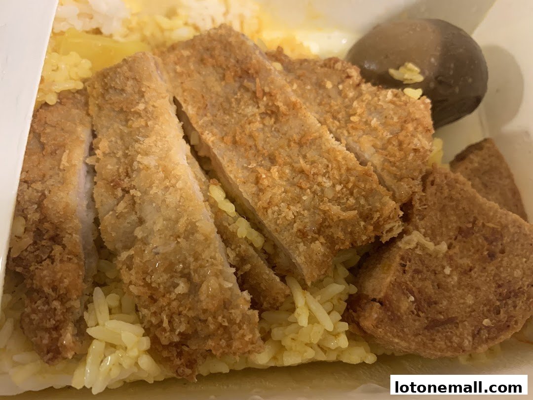 A close-up of Hainanese curry rice with crispy fried pork and a braised egg.
