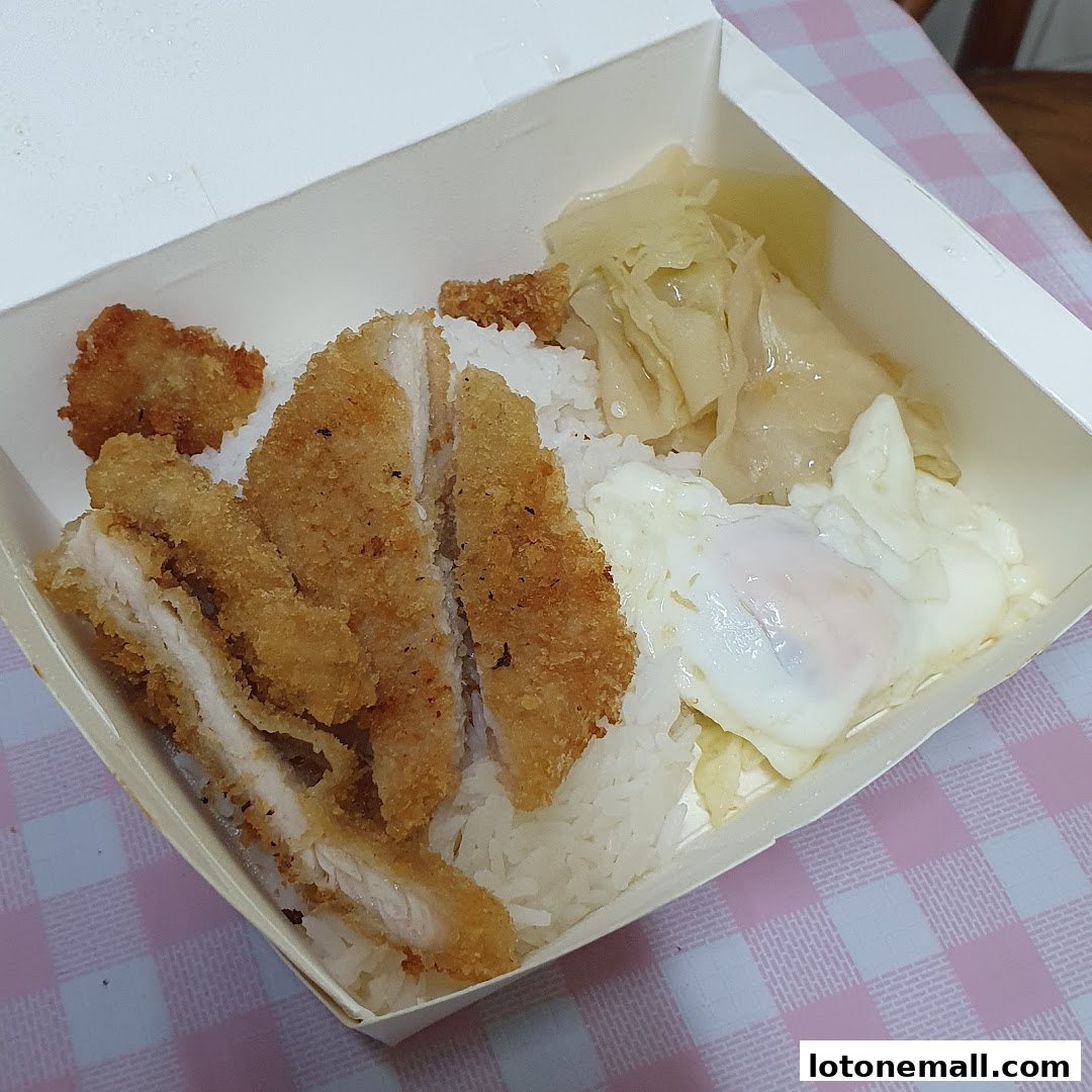 A take-out box filled with Hainanese curry rice, fried chicken, and a sunny-side-up egg.