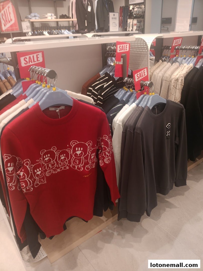 A display of red and grey sweaters with bear prints and other clothing items on hangers.