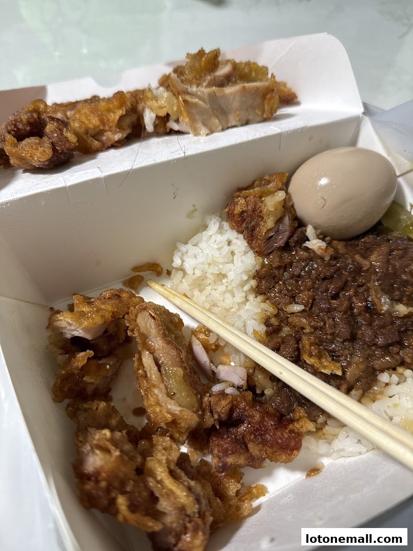 A takeout box filled with fried chicken, rice, braised meat, and a braised egg.