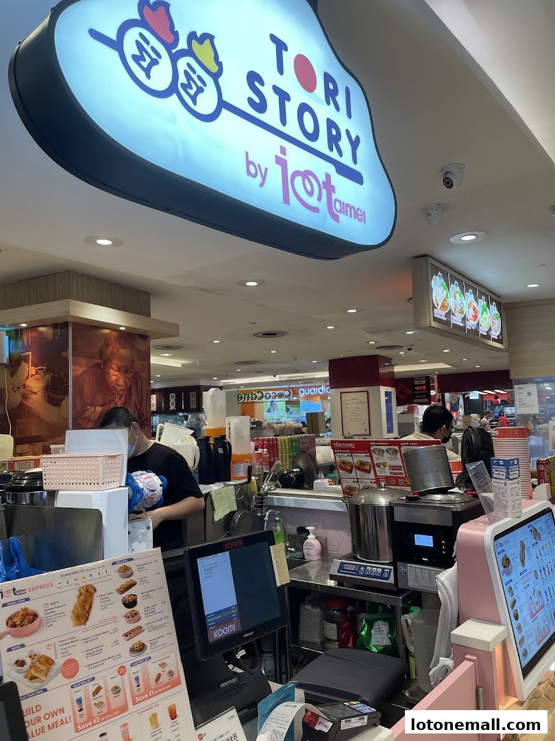 A busy food stall counter with a menu, staff, and various food preparation equipment.