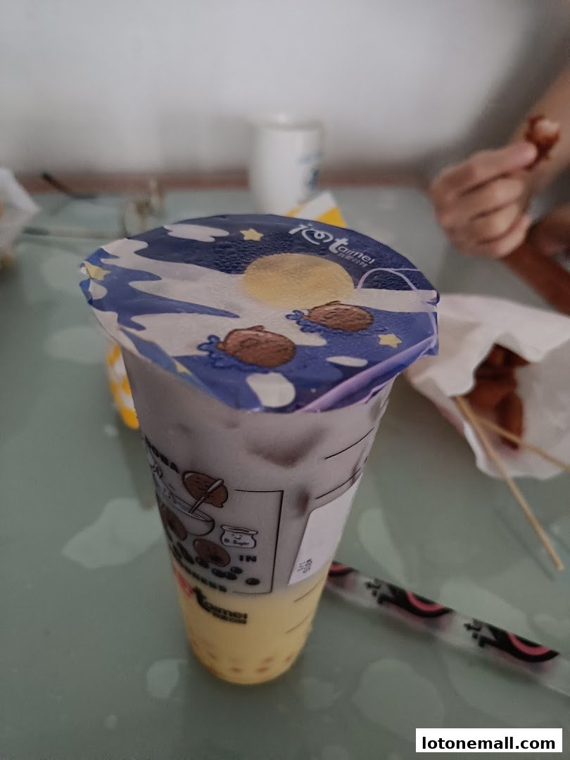 A close-up of a bubble tea with a decorative lid and a straw on a table.