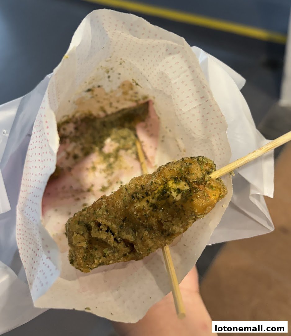 A hand holds a paper bag with a fried chicken skewer covered in green seasoning.