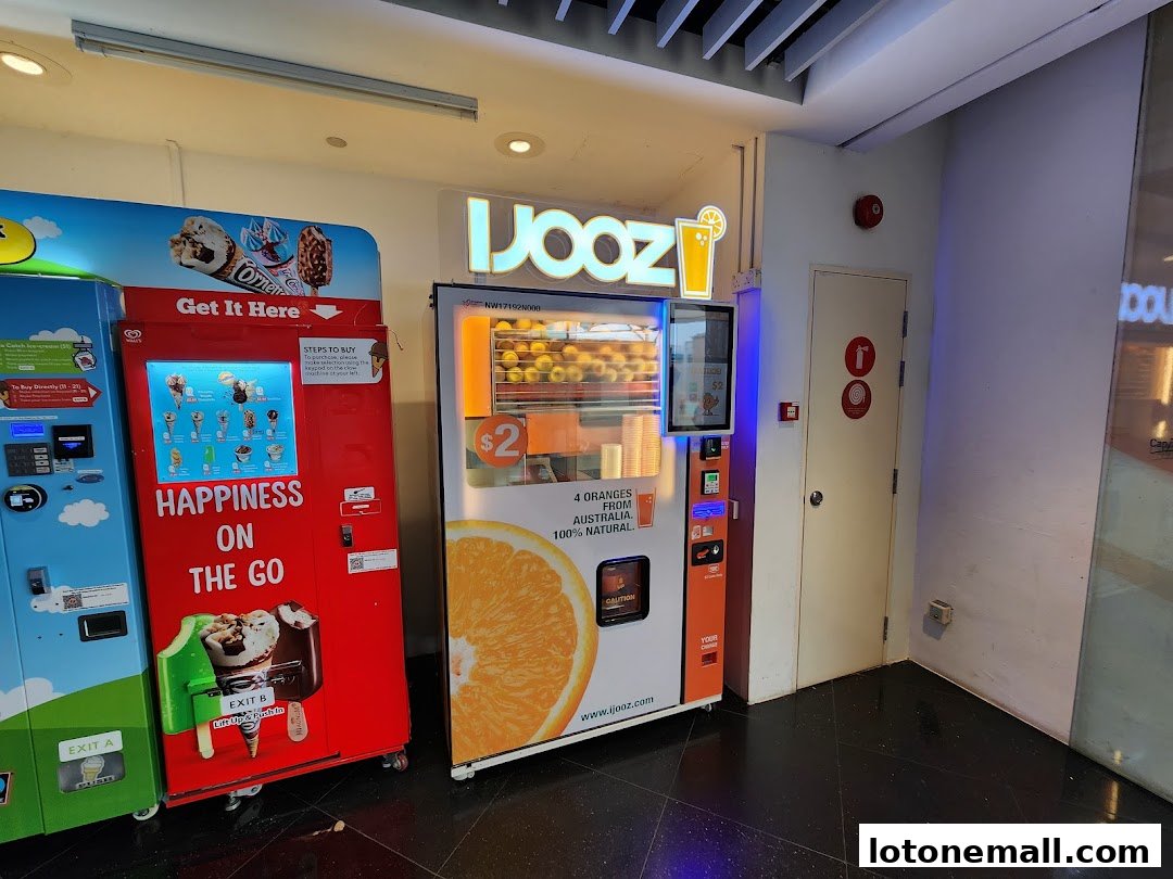 A bright orange and white vending machine dispenses fresh orange juice next to ice cream vending machines.