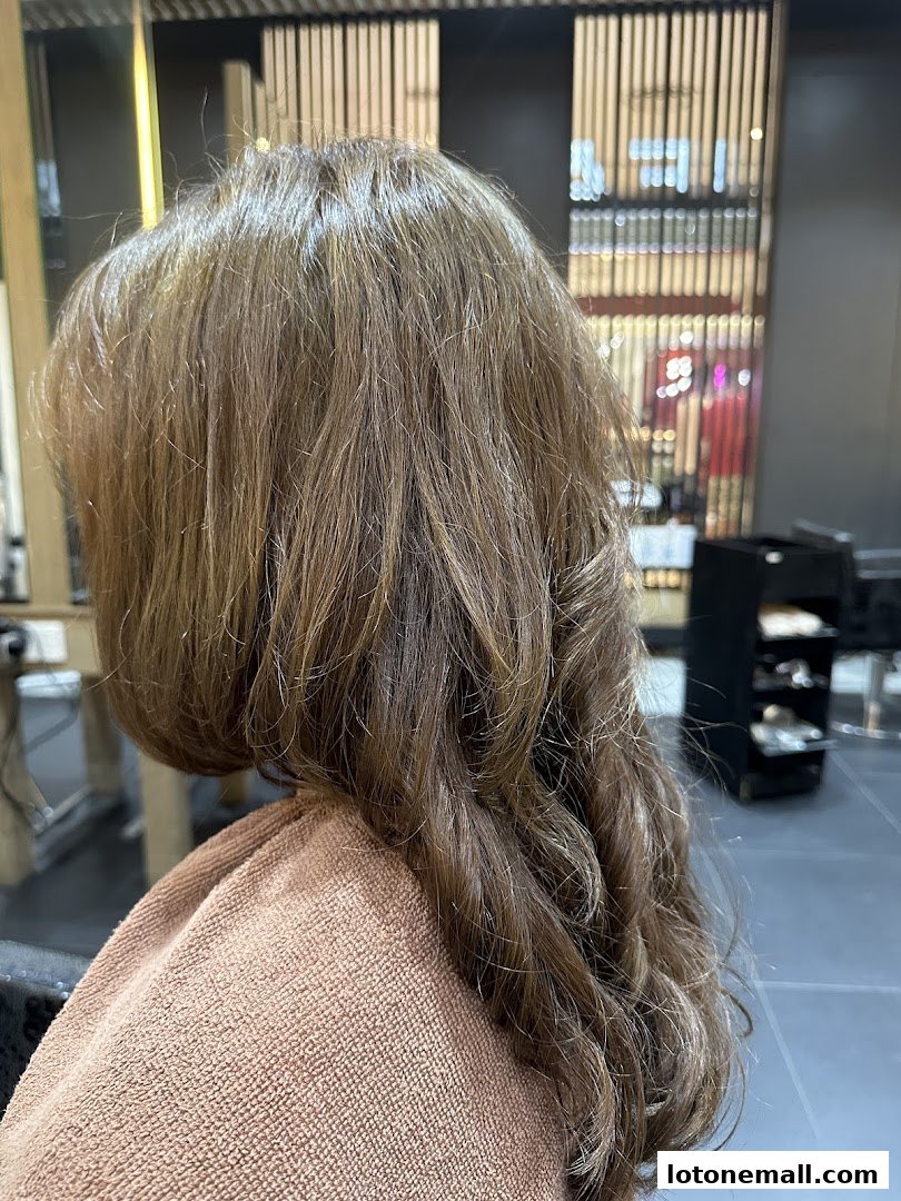 A person's hair is styled with curls and highlights in a salon setting.