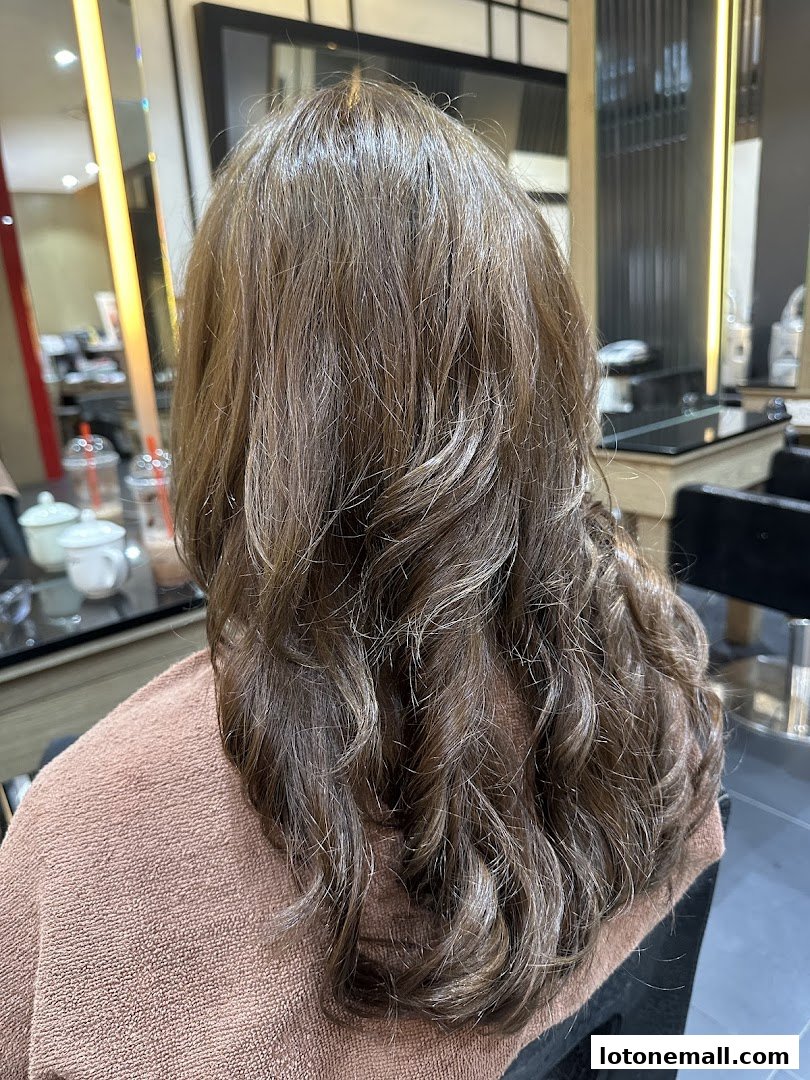 A person's back with styled, wavy brown hair in a salon.