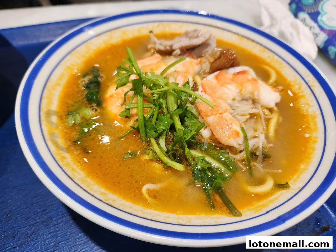 A close-up of a delicious bowl of prawn noodle soup with fresh ingredients.
