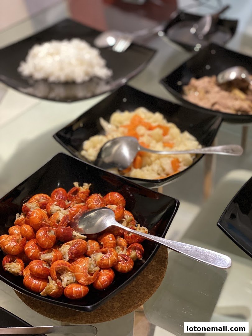 A close-up of several black square bowls filled with various dishes, including crawfish, rice, and other food items.