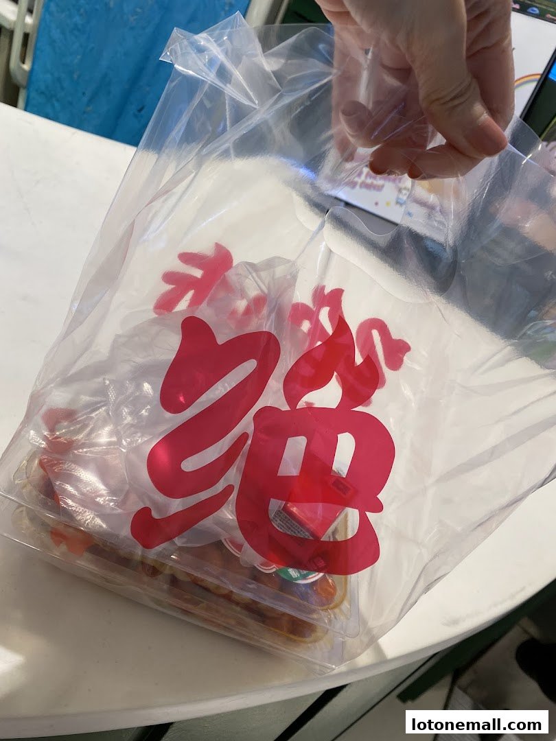 A hand holds a clear plastic bag with red Chinese characters and packaged snacks inside.