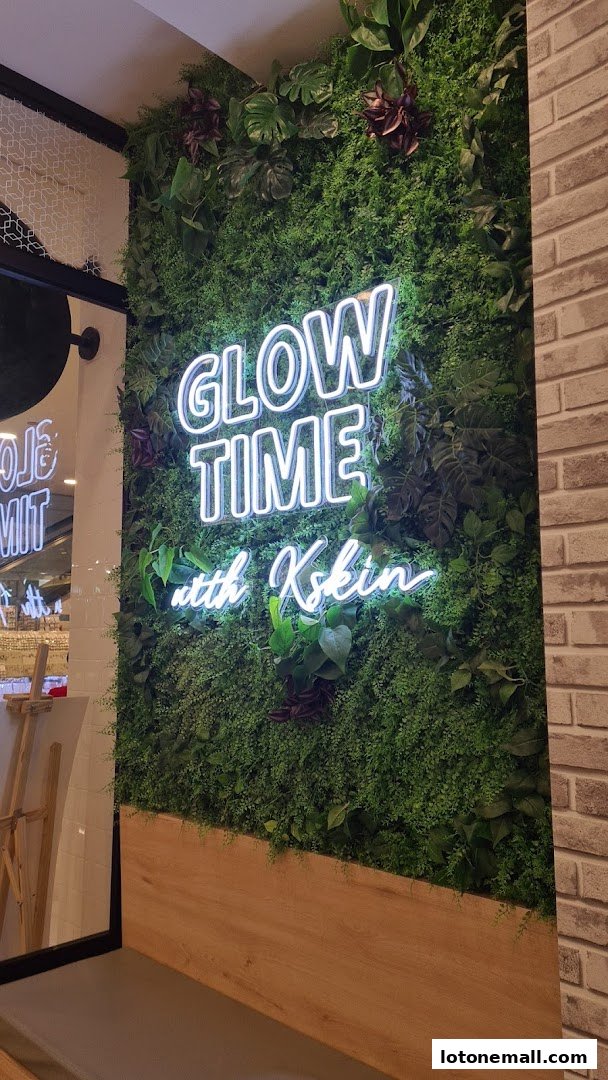 A neon sign saying 'GLOW TIME with Kskin' is displayed on a lush green wall.