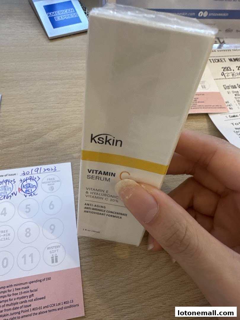 A hand holds a Kskin Vitamin C serum bottle next to a loyalty card.