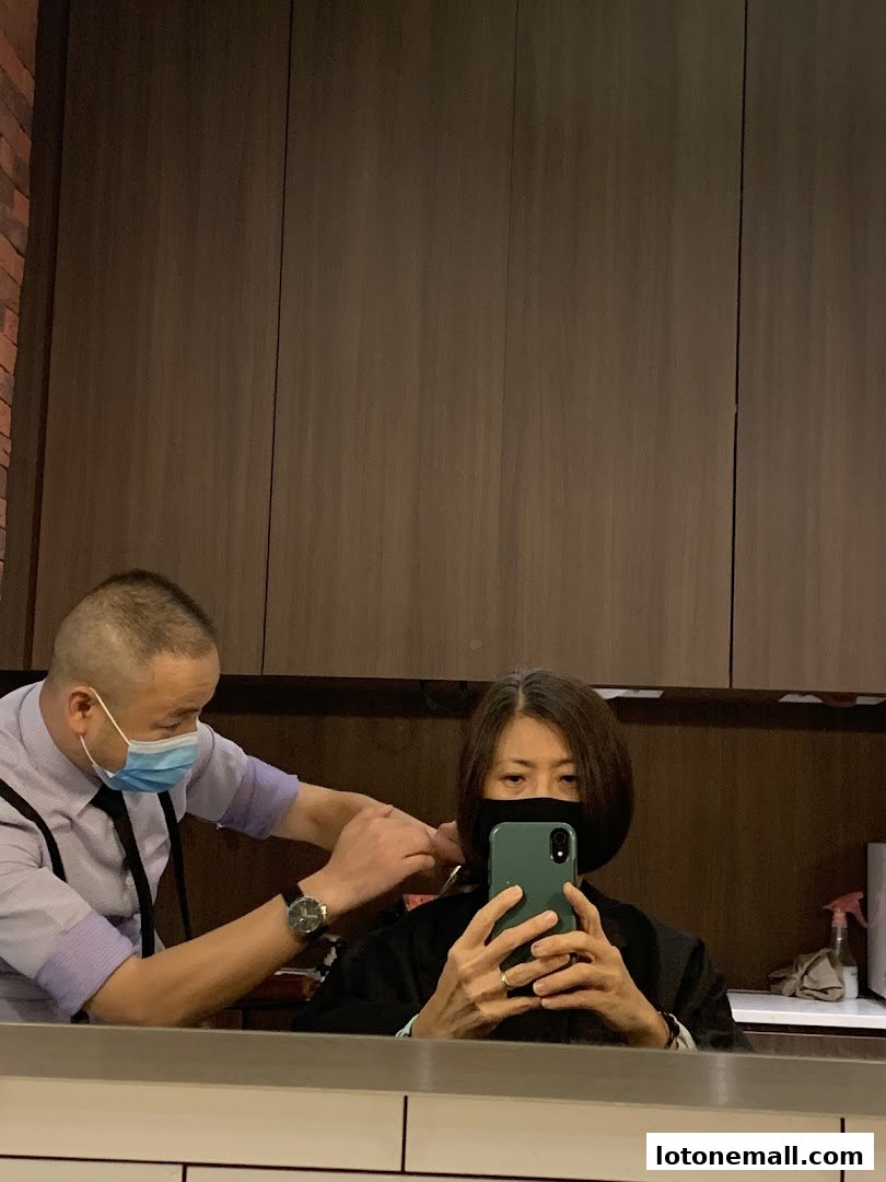 A barber cuts a customer's hair while the customer takes a selfie in the mirror.