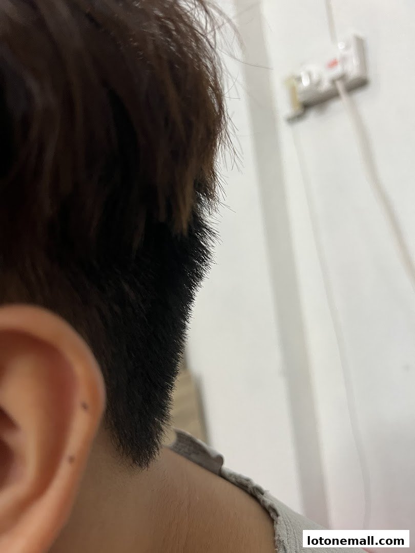 Close-up of a person's ear and the back of their head, with a wall and electrical outlet in the background.