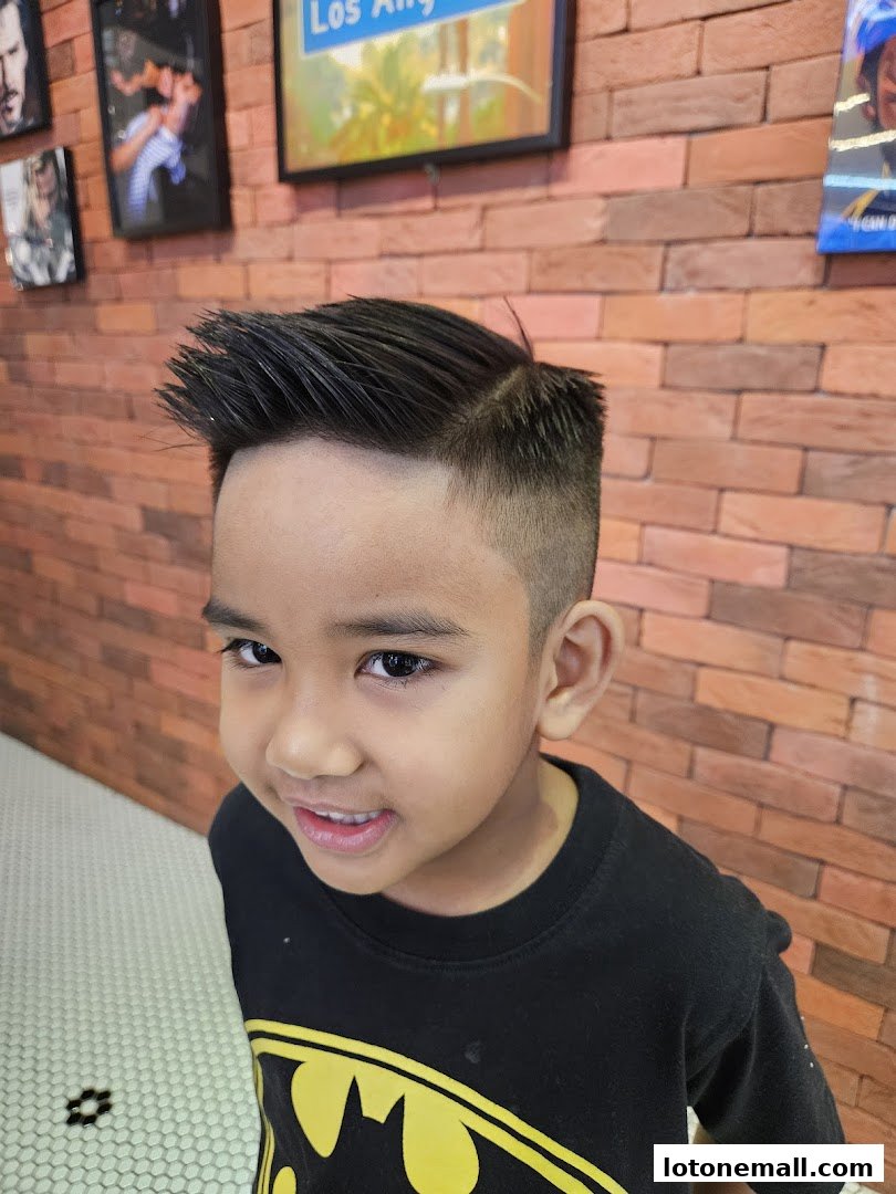 A young boy with a stylish fade haircut smiles at the camera in a barbershop.