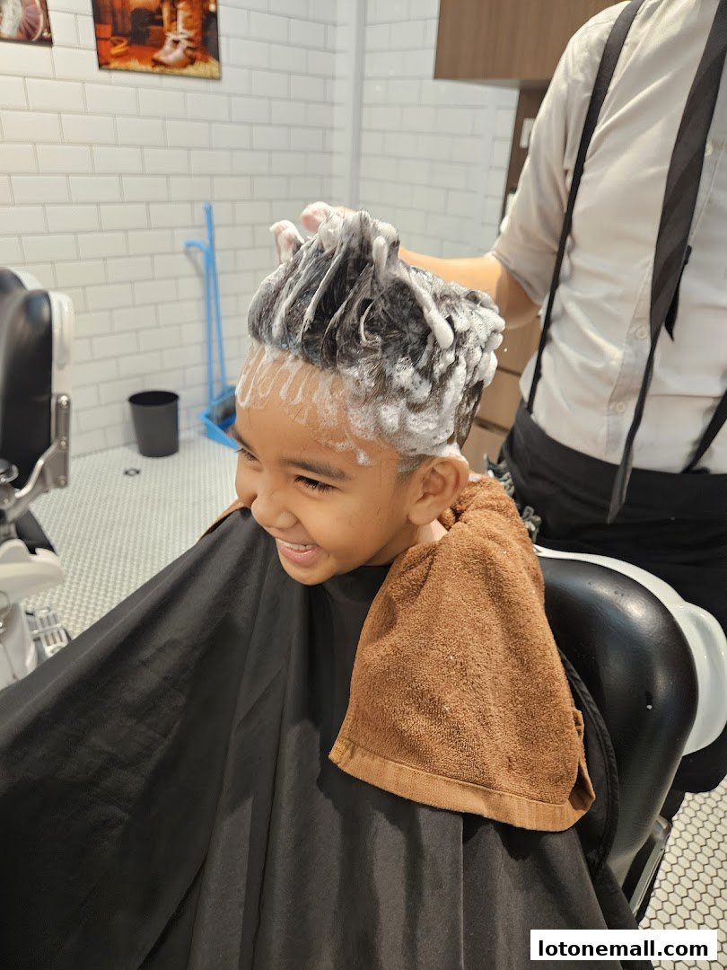 A young boy smiles as he gets his hair washed at LA Barbershop.
