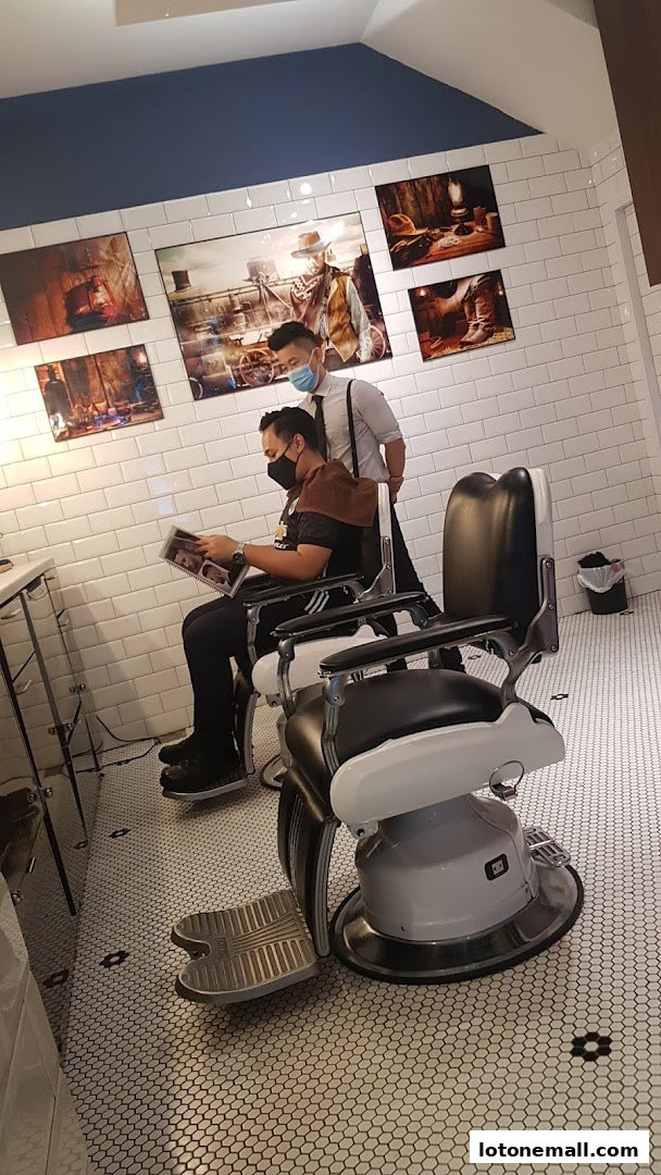A barber is standing behind a customer seated in a barber chair, with artwork on the wall.
