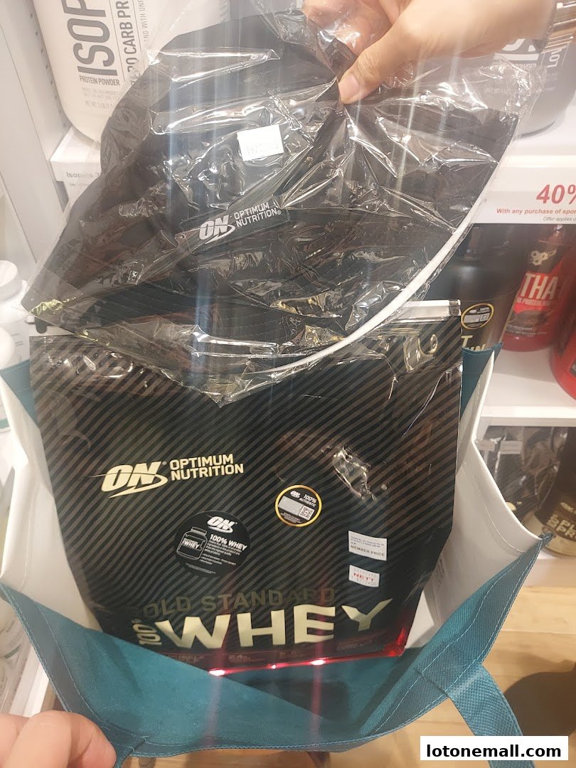 A person holds a large bag of Optimum Nutrition Gold Standard 100% Whey protein powder.