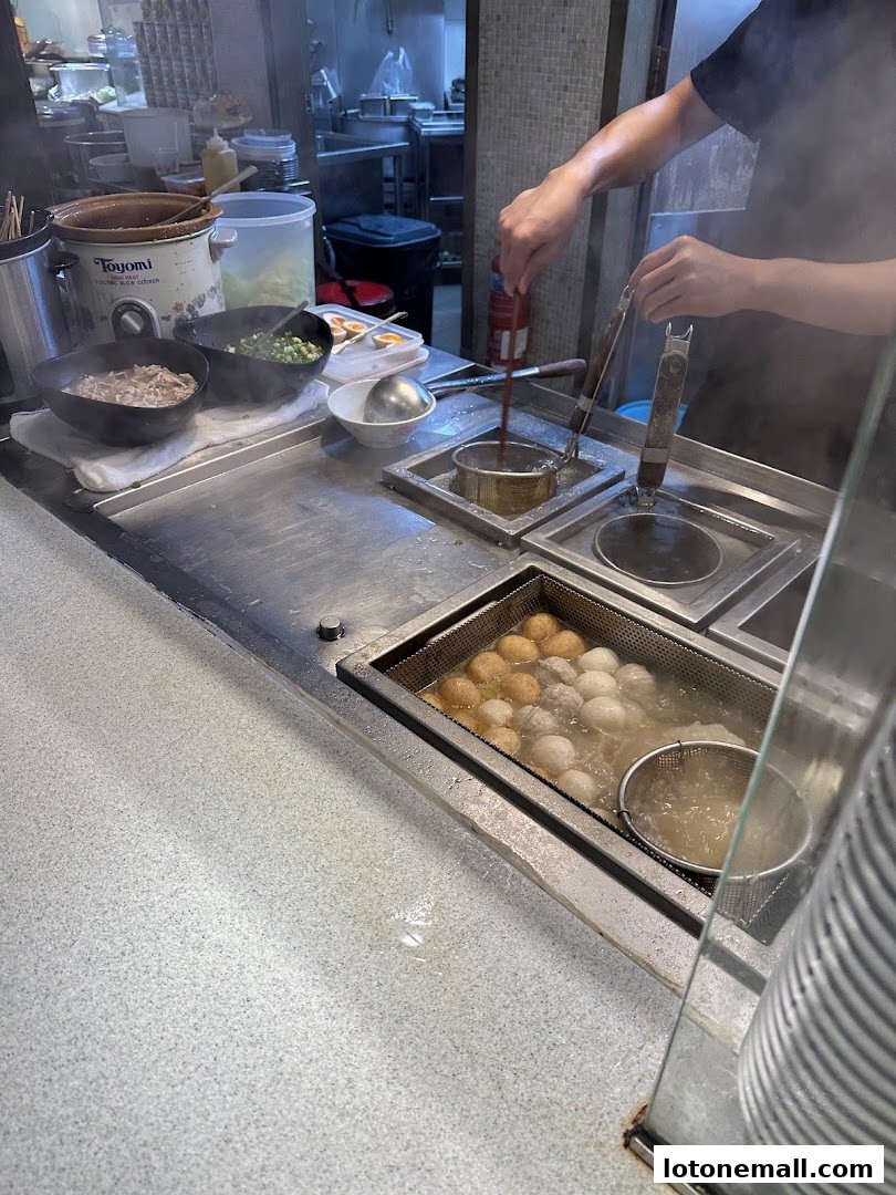 A chef prepares noodles and meatballs in a busy kitchen setting.