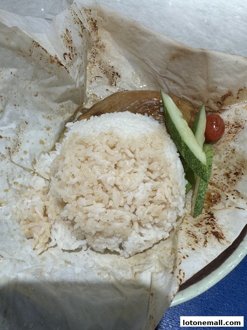A plate of rice with salt-baked chicken, cucumber slices, and a cherry tomato.