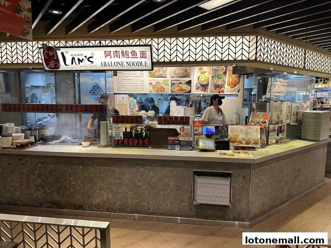 A food stall counter with a menu, staff, and food displays.