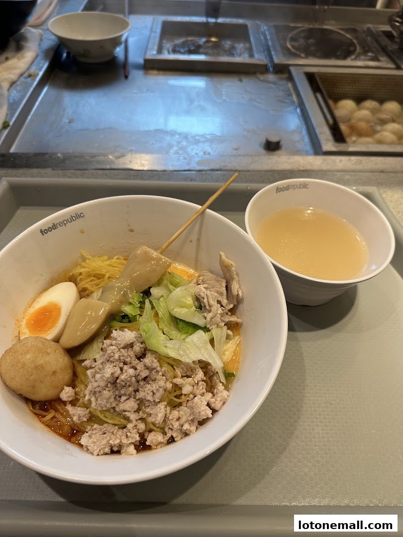 A bowl of noodles with minced meat, egg, and vegetables, served with a side of soup.