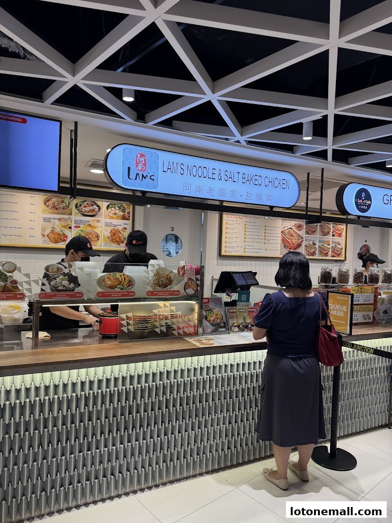 A customer orders at a food stall counter with a menu and food displays.