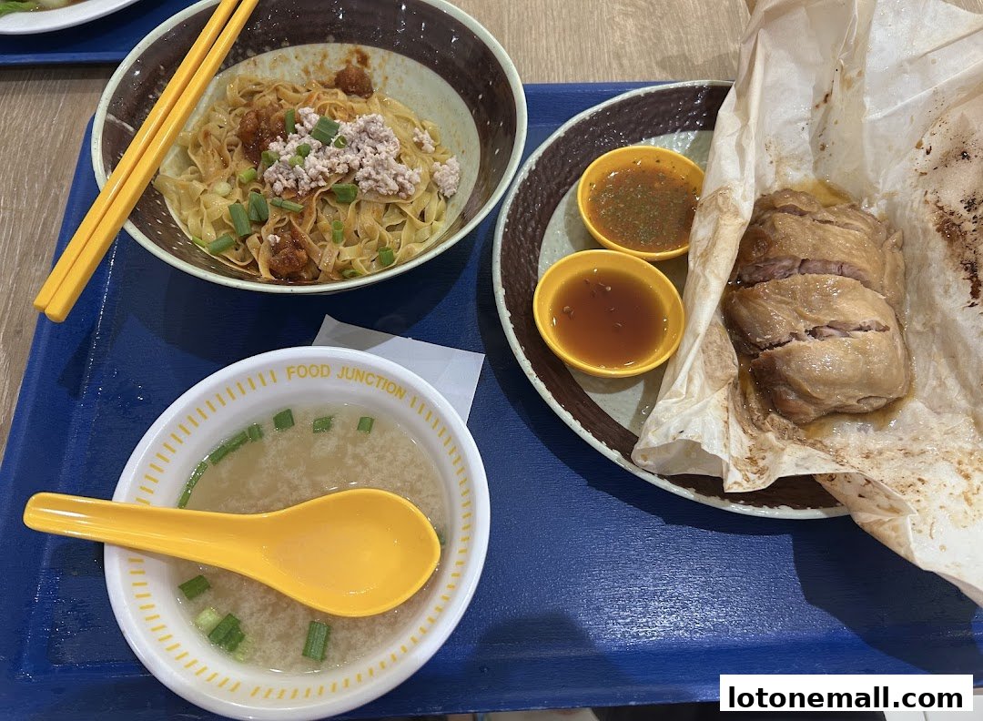 A close-up of a meal featuring noodles, salt-baked chicken, and soup with a spoon.