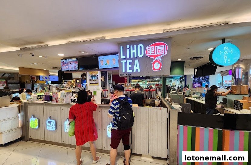 Customers ordering at a LiHO TEA shop counter with illuminated signage and beverage displays.