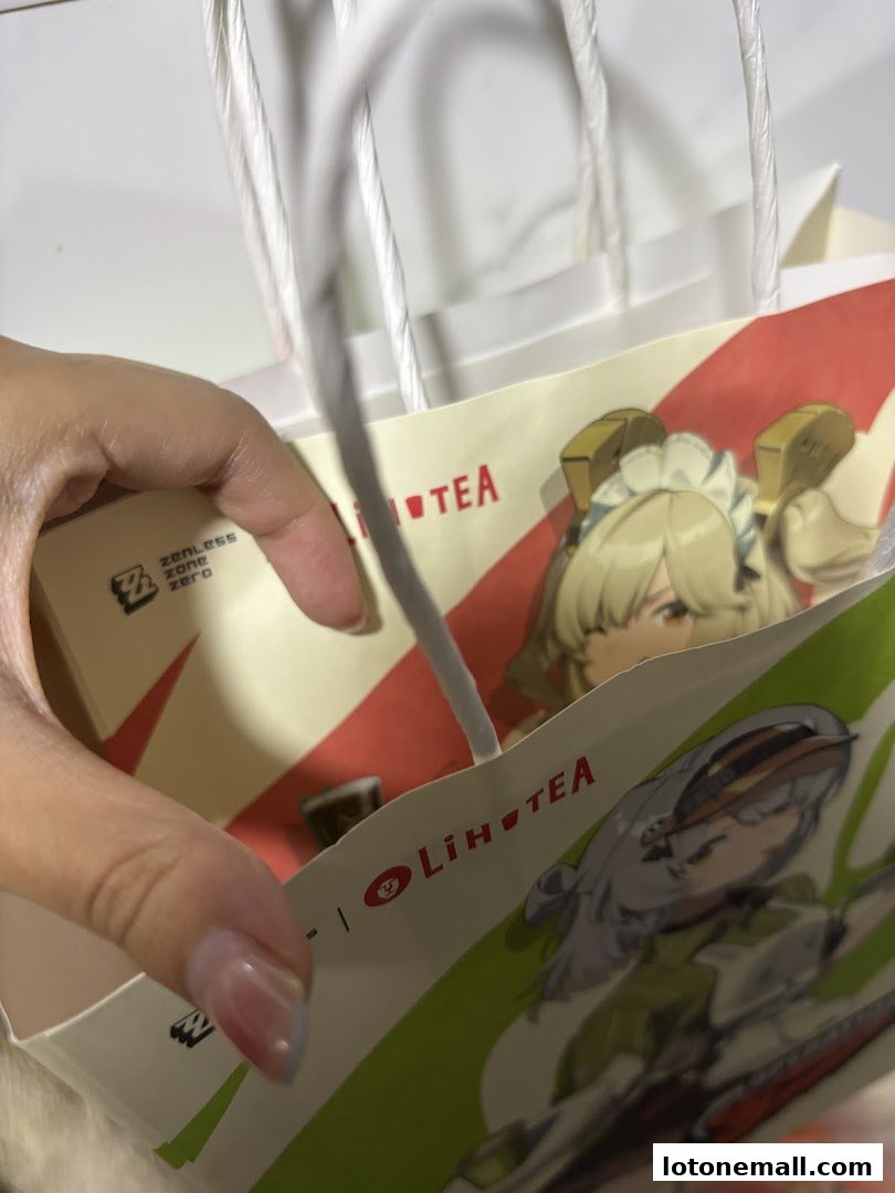 A hand holding a LiHO TEA paper bag with anime characters on it.