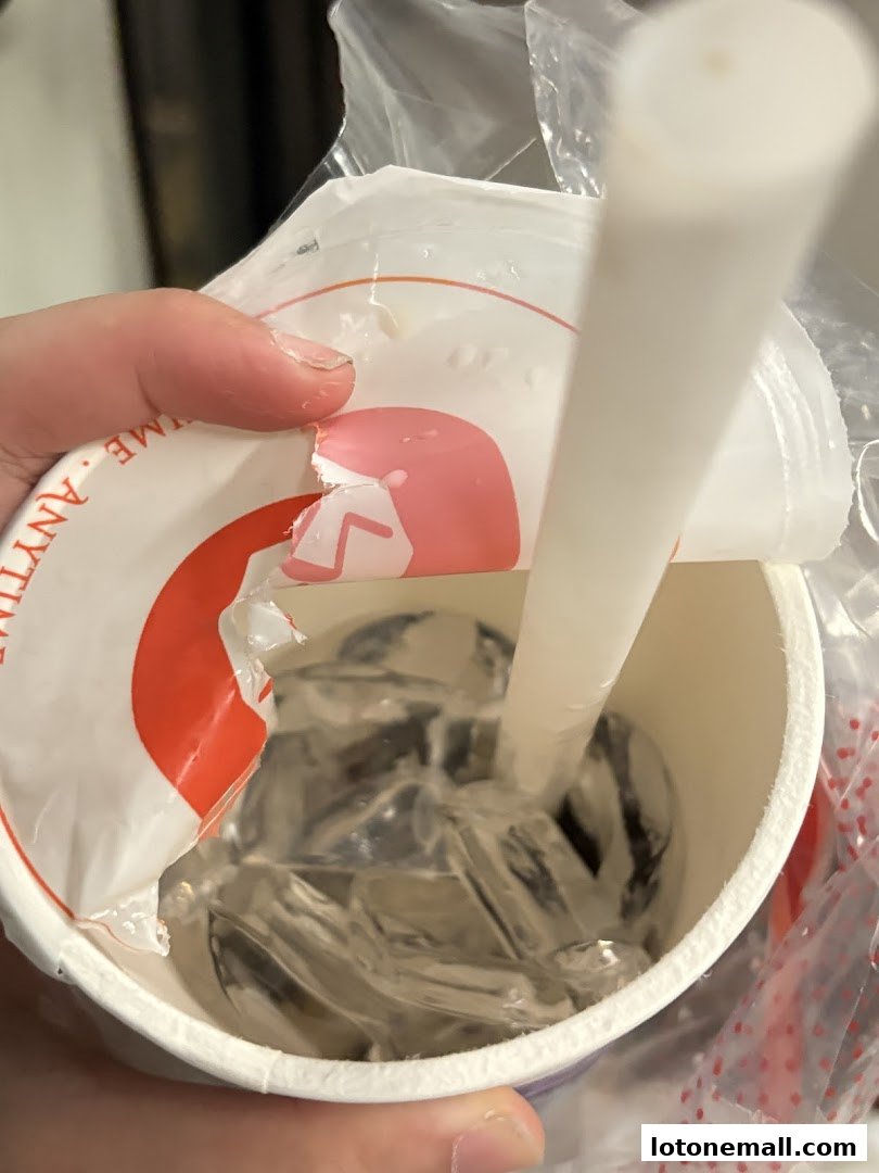 A hand holds a LiHO TEA cup with a straw and ice, partially opened lid.