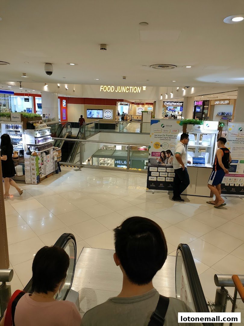 View of a shopping mall interior with escalators and various shops including Food Junction.