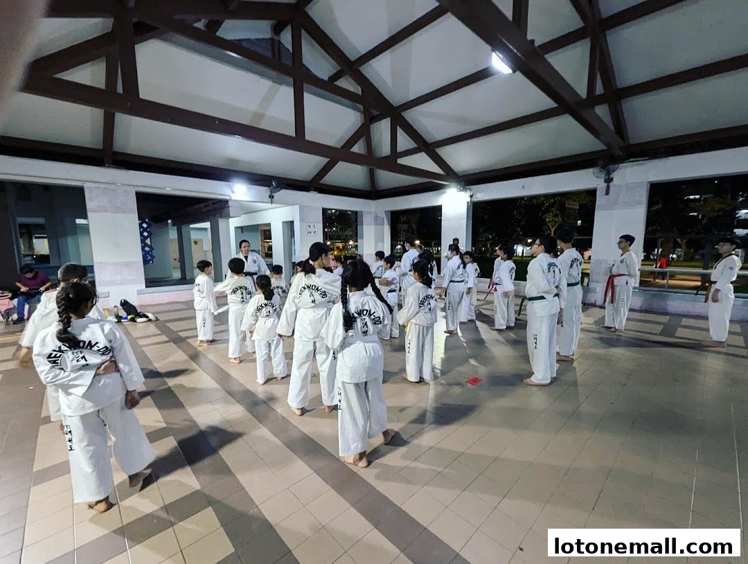 A group of children and adults in Taekwondo uniforms practicing in an open-air pavilion.