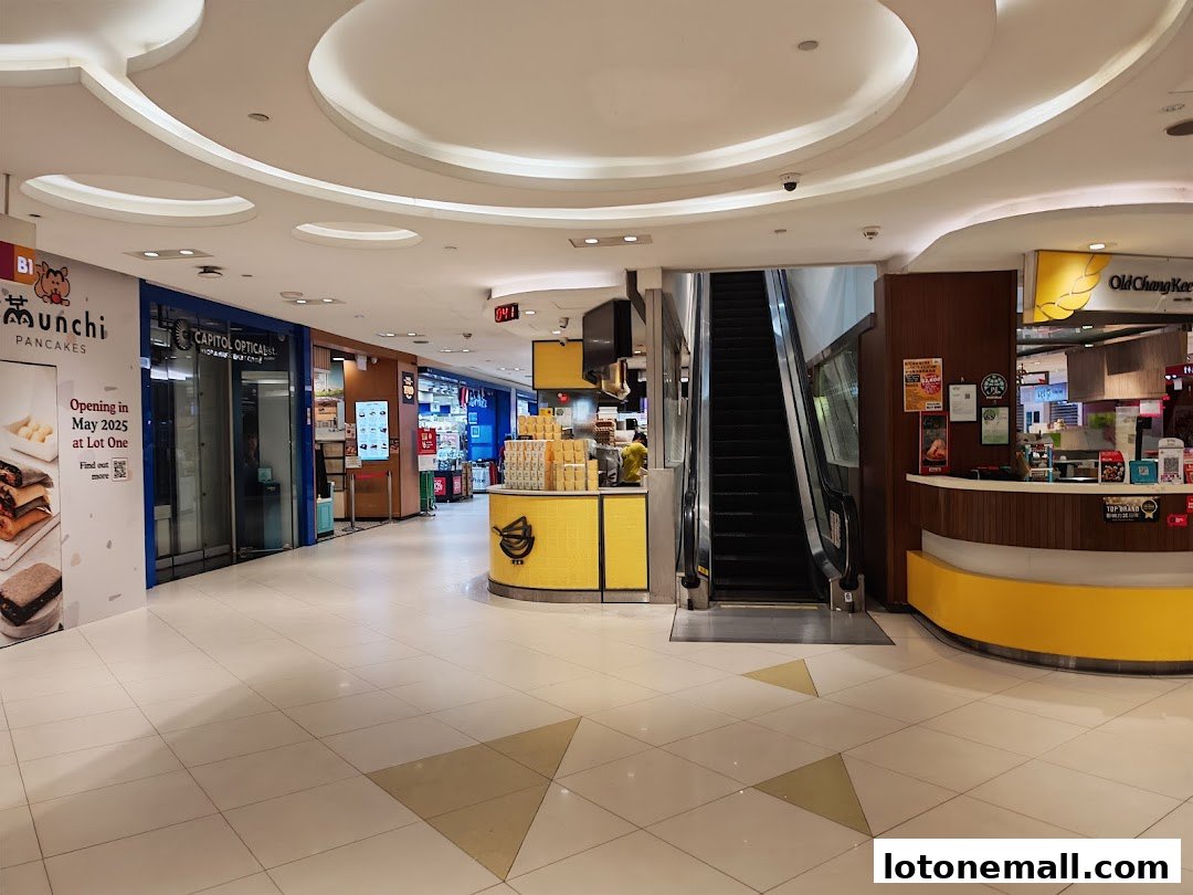 A mall corridor with shops including Capitol Optical and Old Chang Kee, and an escalator.