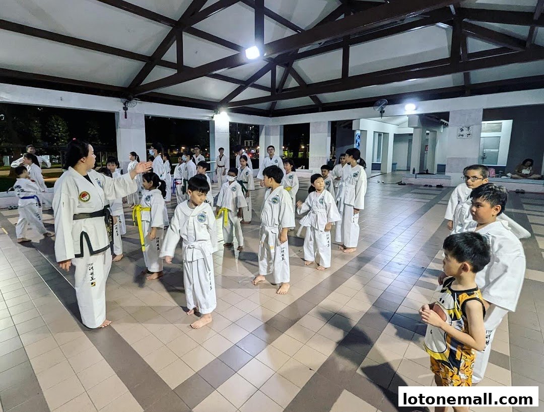 A Taekwondo instructor leads a class of children in an outdoor covered area.