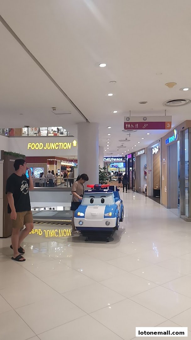 People in a mall hallway with a children's ride-on toy car and a Food Junction sign.