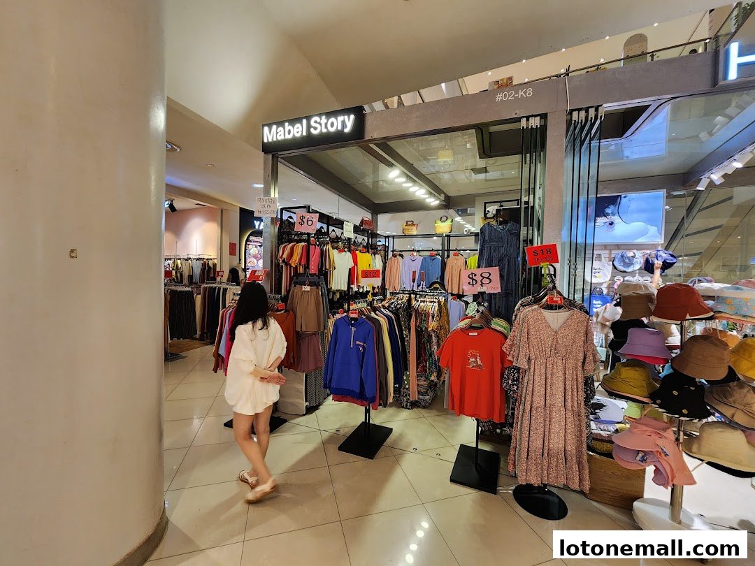 A woman walks past a clothing store displaying various apparel and accessories.