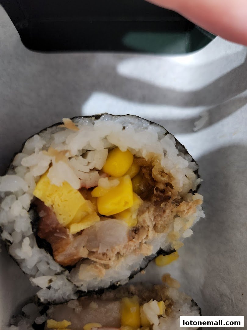 A close-up of a sushi roll with visible ingredients like corn, egg, and tuna.