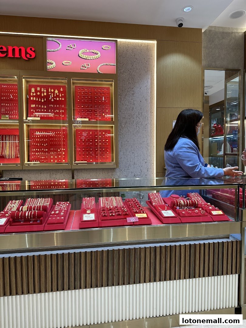 A jewelry store display featuring gold necklaces, bracelets, and rings with a sales associate assisting a customer.