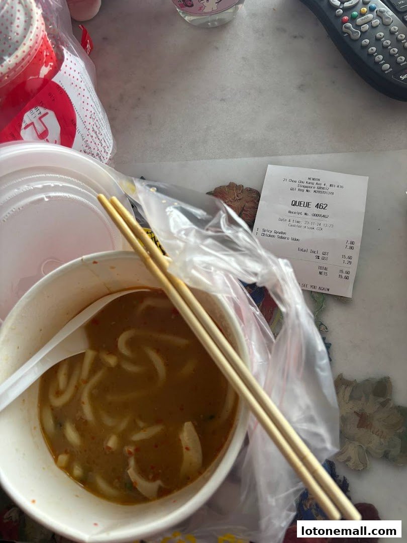 A bowl of udon noodles with chopsticks and a receipt from Mendon.
