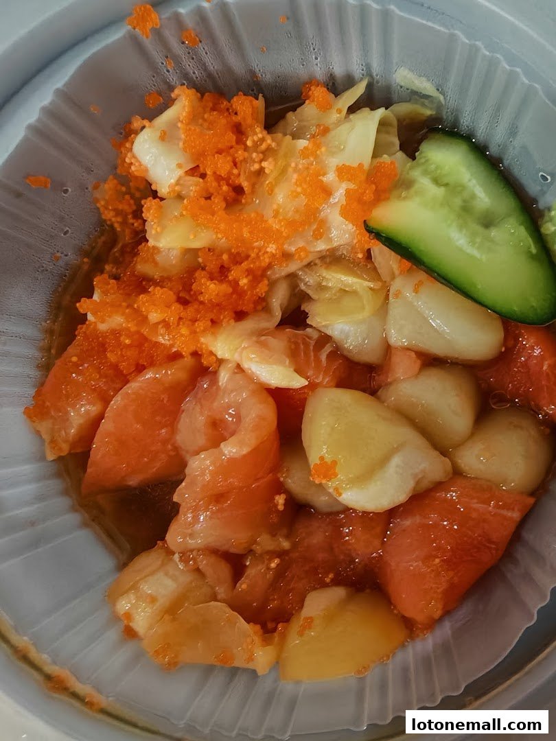 A close-up of a takeaway container filled with salmon, cabbage, and tobiko, garnished with cucumber.